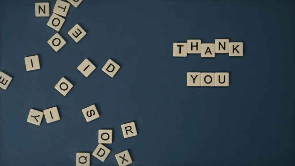 Top view of scattered Scrabble tiles with Thank You spelled out on blue surface.